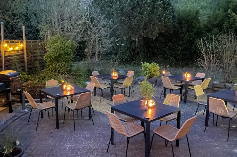 Gemütlicher Garten mit Tischen, Stühlen und Laternen bei Dämmerung.
