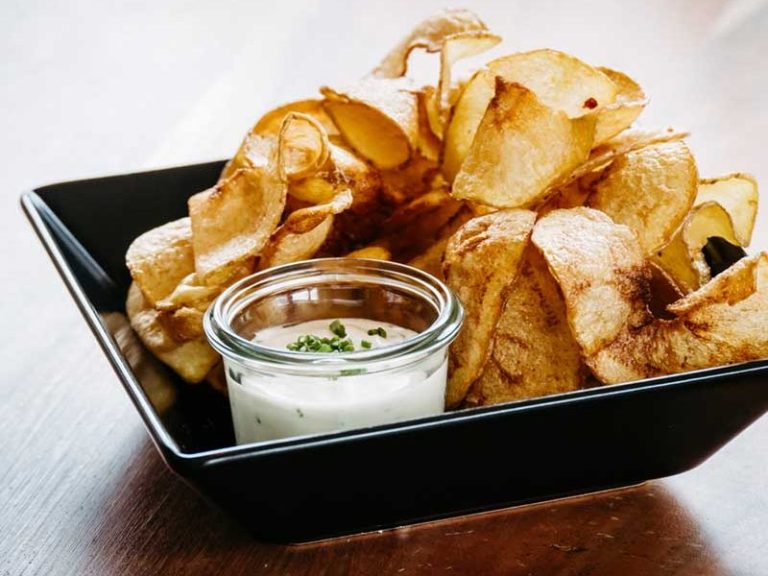 Hausgemachte Kartoffelchips mit einem Becher würziger Dipsoße.