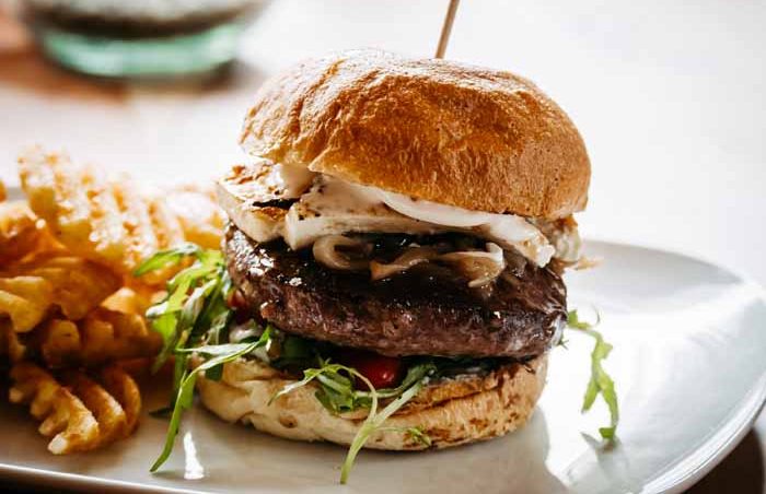 Ein Lammfleisch-Burger mit Schafskäse, Zwiebeln und Pommes frites auf einem Teller.