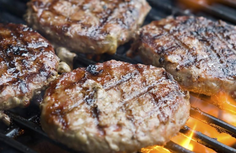 Gegrillte Burger-Patties mit Grillstreifen auf rauchendem Grill.