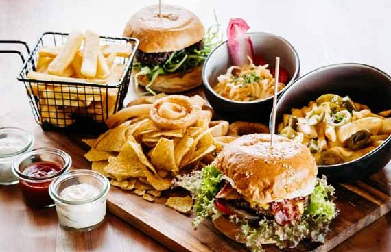 Vielseitige Platte mit Hamburgern, Pommes, Nachos und Dips in verschiedenen Schalen.