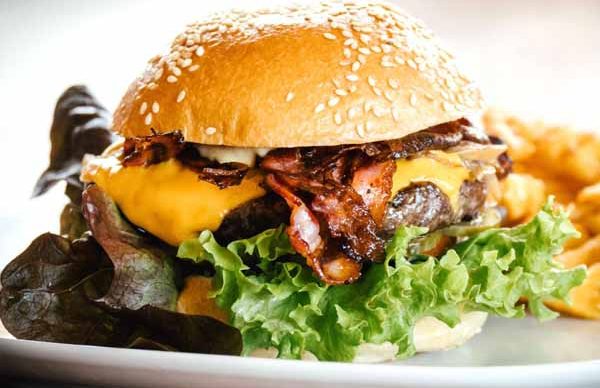 Saftiger Cheeseburger mit Bacon, Salat und Sesambrötchen, serviert mit Pommes.