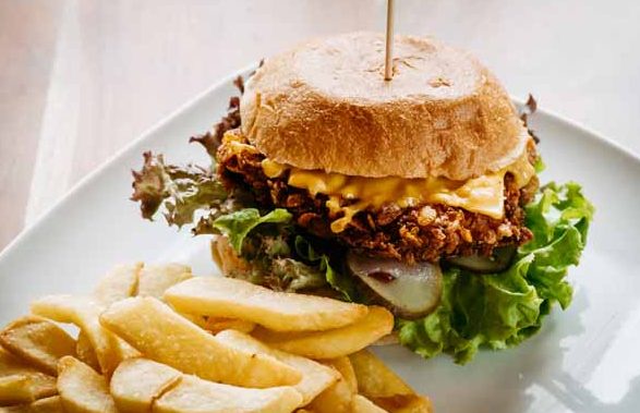 Chicken-Burger mit Käse, Salat und einer Beilage aus Pommes frites auf einem Teller.