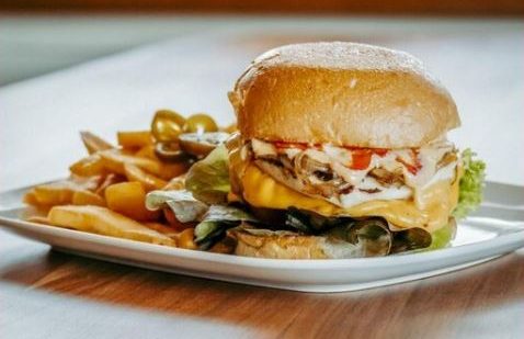 Ein Hamburger mit Käse, Salat, Tomate und Pommes auf einem Teller.