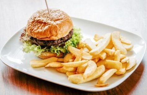 Ein Hamburger auf einem Teller, begleitet von einer Portion Pommes frites.