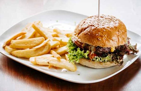Hamburger mit Salat und Käse, serviert mit Pommes frites auf einem weißen Teller.
