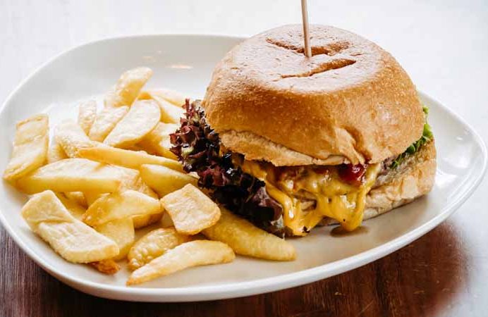 Ein Hamburger mit Käseschmelz und Pommes auf einem Teller.