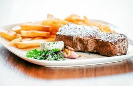 Saftiges Rindersteak mit Kräuterbutter, Pommes frites und frischem Gemüse.
